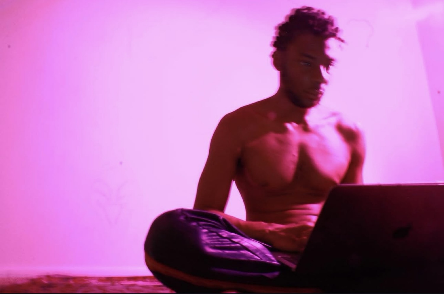 Kydale Outley sitting with a laptop in magenta light.