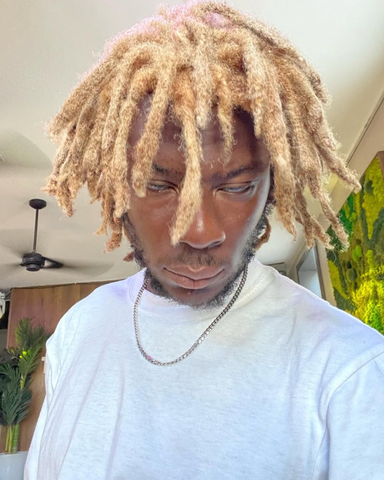 Kydale Outley looking down, blonde locs, a white shirt.